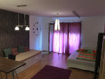 Design-os hálószoba, jobbra egy franciaágy, balra egy kanapé, az egész szobát hangulatos fények jellemzik, melyek a lila függönyön keresztül szűrődnek be.